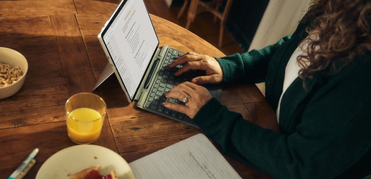 Woman typing on laptop at wooden table with breakfast.